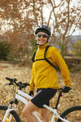 Happy woman standing with mountain bike near trees in forest - EBSF04320