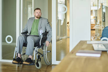 Businessman sitting in wheelchair and entering from door at office - DSHF01480