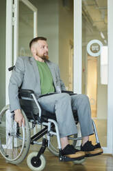 Businessman sitting in wheelchair near glass door - DSHF01481
