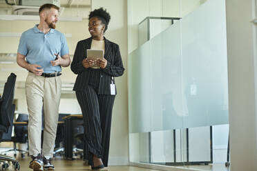 Smiling businesswoman holding tablet PC and walking in office - DSHF01488