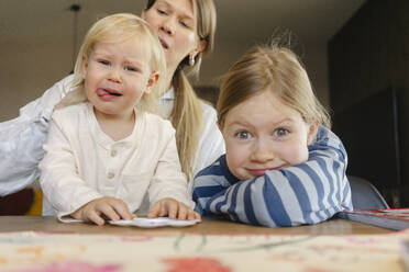 Verspielte Schwestern mit Gesichtsausdrücken und Mutter im Hintergrund zu Hause - SEAF02073