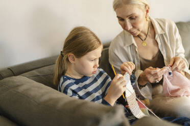 Focused girl learning to knit with grandmother at home - SEAF02082