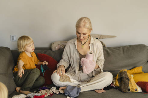 Großmutter strickt mit ihrem Enkel auf dem Sofa zu Hause - SEAF02088
