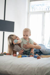 Mother and son playing toy blocks on bed at home - JOSEF22397