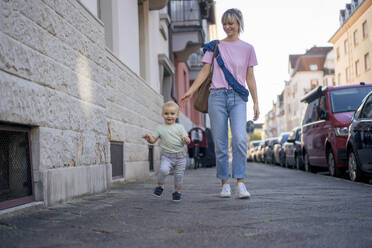 Mother and son walking together on sidewalk in city - JOSEF22398