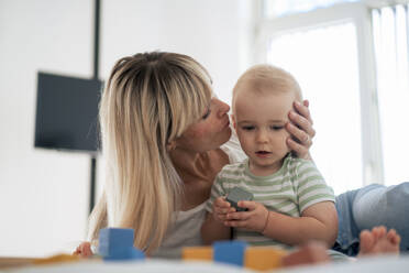 Mother kissing son playing with toy blocks on bed at home - JOSEF22399