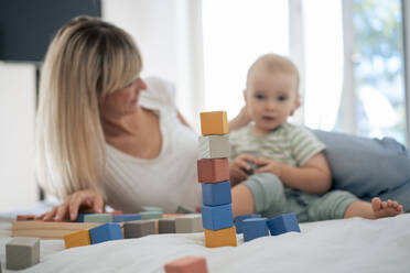 Stack of toy blocks with mother and son on bed at home - JOSEF22401