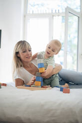 Mother and son playing with toy blocks game on bed at home - JOSEF22402