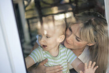 Mother embracing son seen through glass window - JOSEF22405