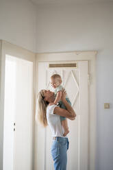 Happy woman enjoying with son near doorway at home - JOSEF22407