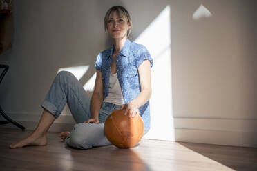 Woman sitting with ball near wall at home - JOSEF22408