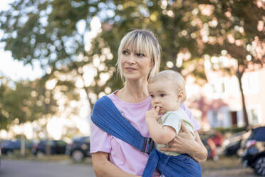 Contemplative woman carrying son in baby sling - JOSEF22418