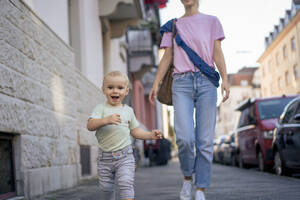 Happy boy running with mother on sidewalk in city - JOSEF22423