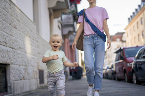 Happy boy running with mother on sidewalk in city - JOSEF22423