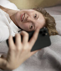 Lächelnde Frau benutzt Smartphone zu Hause - MBLF00185