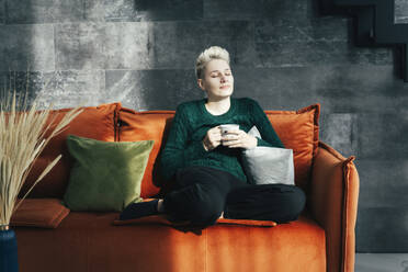 Woman holding coffee mug and relaxing on sofa at home - OLRF00004