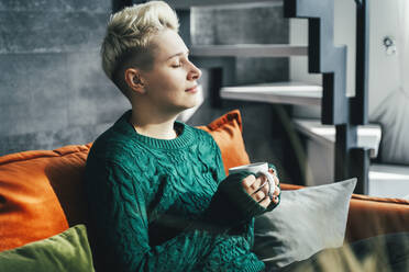 Young woman wearing green sweater and holding coffee mug in hand at home - OLRF00006