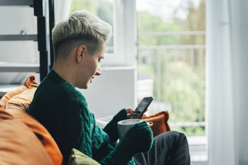 Junge Frau, die ein Smartphone benutzt und zu Hause sitzt - OLRF00008