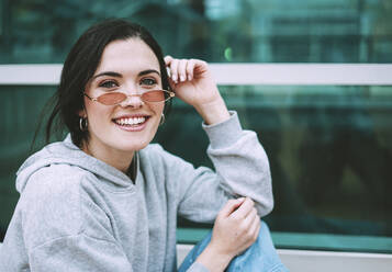 Smiling woman wearing gray hoodie and retro sunglasses - SVCF00447