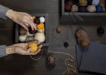 Hands of woman choosing balls of yarn on table - MBLF00186