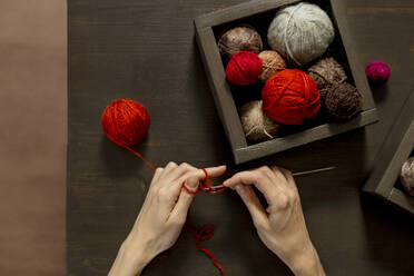 Hands of woman knitting with red yarn on table - MBLF00188