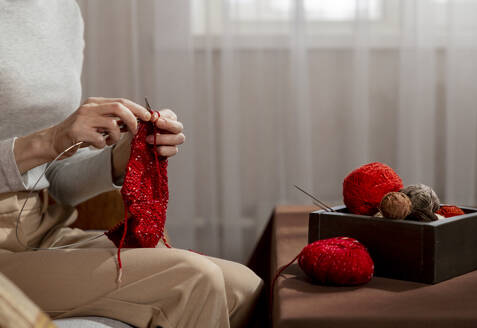 Ältere Frau strickt mit rotem Garn am Tisch zu Hause - MBLF00195