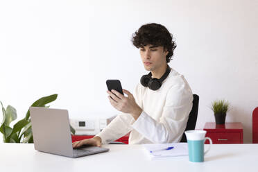 Businessman using smart phone at desk in home office - LMCF00708