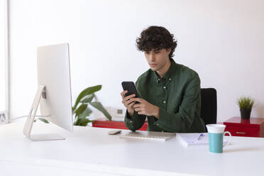 Businessman using mobile phone sitting at desk in home office - LMCF00724