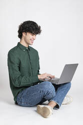 Lächelnder Mann mit Laptop vor einem weißen Hintergrund - LMCF00727
