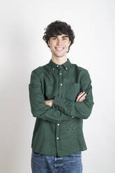 Smiling confident man standing with arms crossed against white background - LMCF00728