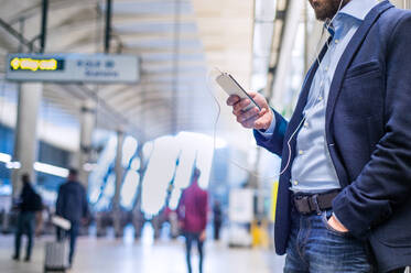 Close up of unrecognizable hipster businessman with smartphone standing on subway station listening music - HPIF35891