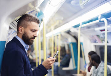 Junger gut aussehender Geschäftsmann mit Smartphone in der U-Bahn - HPIF35892