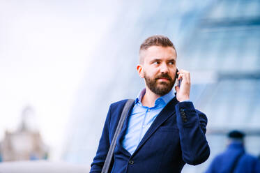 Hipster manager holding a smart phone, making a phone call, City Hall, London - HPIF35905