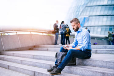 Hipster-Manager sitzt an einem sonnigen Tag auf einer Treppe und arbeitet an einem Tablet, London, City Hall - HPIF35911