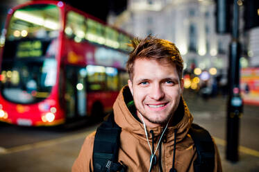 Young hipster man with earphones, listening music, walking in the streets of London at night - HPIF35924