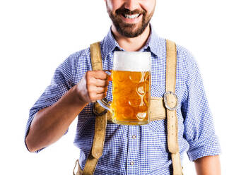 Unrecognizable young man in traditional bavarian clothes holding a mug of beer. Oktoberfest. Studio shot on white background, isolated. - HPIF35934
