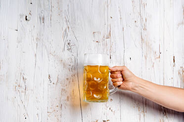 Hand eines nicht erkennbaren Mannes, der einen Bierkrug hält. Oktoberfest. Studioaufnahme auf weißem Holzhintergrund. Kopierraum. - HPIF35938