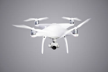 Fliegende Hubschrauberdrohne mit angehobenem Fahrwerk und Kamera, Studioaufnahme auf grauem Hintergrund. - HPIF35946