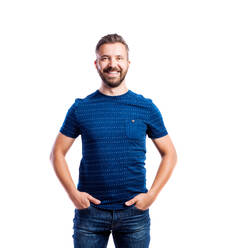 Junger gutaussehender Hipster-Mann in blauem T-Shirt, Hände in den Taschen, Studioaufnahme auf weißem Hintergrund, isoliert - HPIF35954