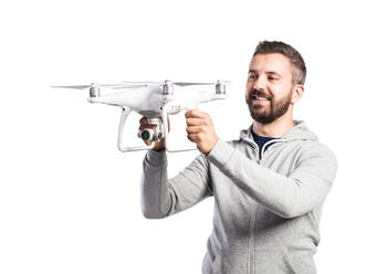 Junger Hipster-Mann in grauem Sweatshirt, der eine Drohne mit Kamera hält, Studioaufnahme auf weißem Hintergrund, isoliert. - HPIF35959