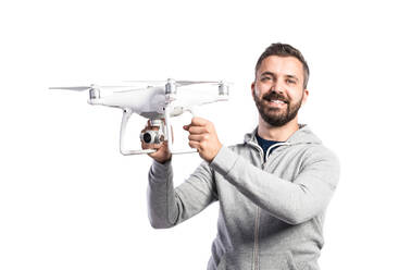 Junger Hipster-Mann in grauem Sweatshirt, der eine Drohne mit Kamera hält, Studioaufnahme auf weißem Hintergrund, isoliert. - HPIF35960