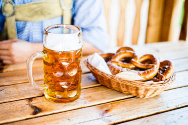 Unbekannte Männer in traditioneller bayerischer Kleidung sitzen am Tisch mit einem Krug Bier, Brezeln im Weidenkorb, Oktoberfest. - HPIF35970