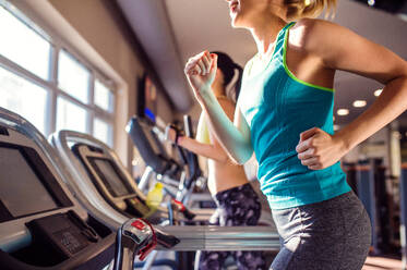 Zwei attraktive, fitte Frauen in Sportkleidung laufen auf Laufbändern in einem modernen Fitnessstudio - HPIF35977