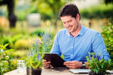 Gardener sitting at the table, holding a clipboard, managing supplies, green sunny nature - HPIF35989