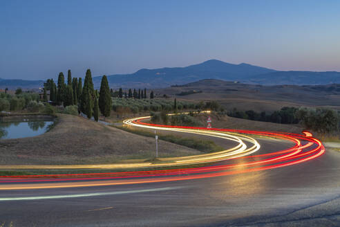 Blick auf Autolichter in der toskanischen Landschaft bei Pienza in der Abenddämmerung, Pienza, Provinz Siena, Toskana, Italien, Europa - RHPLF29939