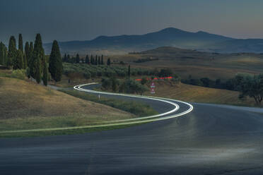 Blick auf Autolichter in der toskanischen Landschaft bei Pienza in der Abenddämmerung, Pienza, Provinz Siena, Toskana, Italien, Europa - RHPLF29942