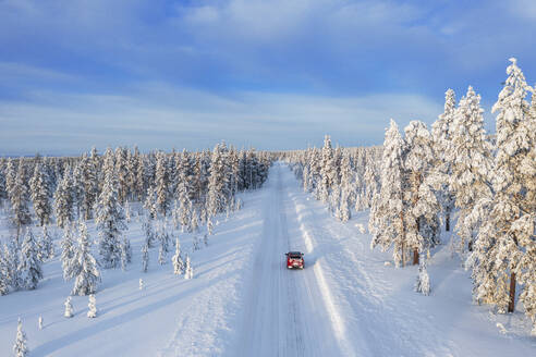 Drohnenansicht eines Autos, das auf einer leeren und gefrorenen Straße in der weißen Landschaft von Schwedisch-Lappland fährt, Schweden, Skandinavien, Europa - RHPLF30278