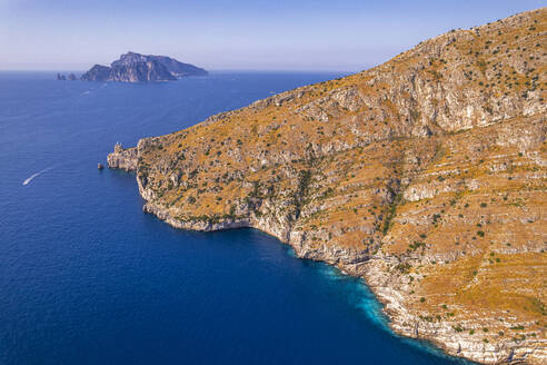 Luftaufnahme einer felsigen Küste mit Blick auf das blaue Wasser des Tyrrhenischen Meeres und der Insel Capri im Hintergrund, Amalfiküste, Provinz Neapel, Region Kampanien, Süditalien, Italien, Europa - RHPLF30290