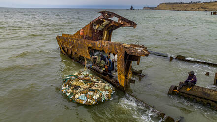 Männer zerlegen ein Boot am Strand von Shipwreck, Bucht von Santiago, Luanda, Angola, Afrika - RHPLF30547