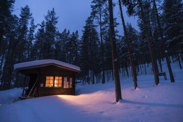 Blockhaus mit Feuer im Inneren, Winter, Lemmenjoki Nationalpark, Finnland, Europa - RHPLF31471